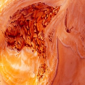 Abstract image of swirling orange, copper, and peach tones with cracked, flaking textures and layered forms, creating a molten, organic surface that evokes eroded rock, heat, and flowing mineral deposits.