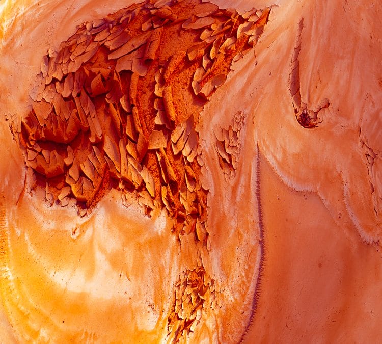 Abstract image of swirling orange, copper, and peach tones with cracked, flaking textures and layered forms, creating a molten, organic surface that evokes eroded rock, heat, and flowing mineral deposits.