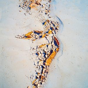 Abstract image of a vertical, river-like fracture of cracked white and ochre textures running through a pale blue surface, with peeling layers and granular details that evoke eroded stone, dried clay, and a weathered geological channel.