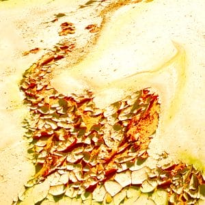 Abstract image of sunlit yellow and cream textures with cracked, peeling layers in red and green, forming a flowing diagonal band that evokes eroded desert stone, wind-worn surfaces, and glowing geological strata.