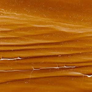 Abstract image of layered amber and golden-brown textures with soft horizontal striations and fine white fissure lines, evoking sedimentary rock, flowing resin, and a warm, time-worn surface.