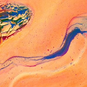 Abstract image of a glowing orange and coral surface crossed by a sinuous blue-violet channel, with cracked, layered textures and fragmented shapes that resemble eroded rock, flowing pigment, and a river cutting through sunlit terrain.