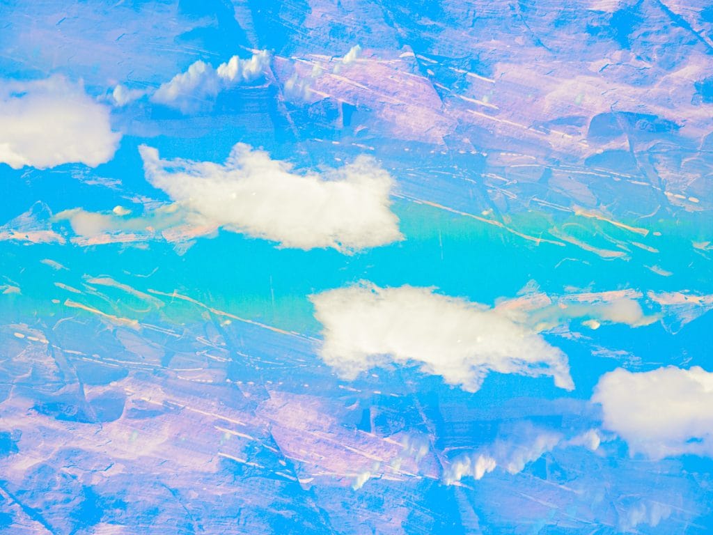 Abstract, mirrored sky composition with soft white clouds floating across bands of turquoise and blue, layered with pastel lavender textures and subtle linear marks creating a sense of movement and symmetry.